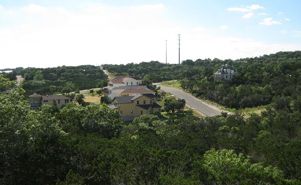 Central Texas homes across a cedar and live oak hillside under big sky, the kind of established neighborhood found across Cedar Park, TX 78613