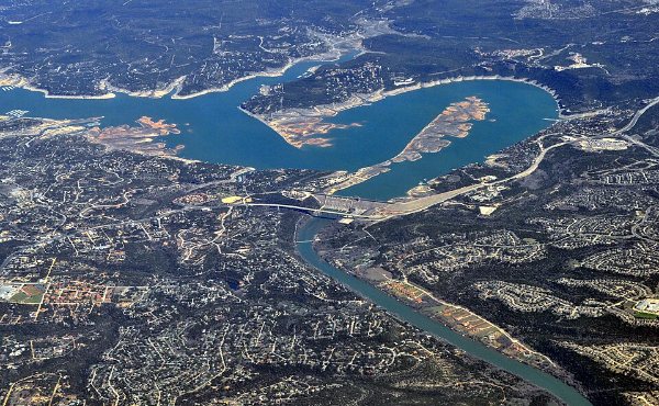 Aerial view of Mansfield Dam and Lake Travis winding through the hillside neighborhoods of Hudson Bend, TX 78734